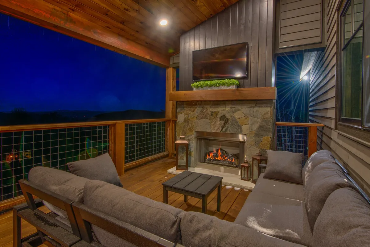 An outdoor lounging space with a stone fireplace, comfortable seating, and a large TV under a wooden ceiling—ideal for gatherings, movie nights, or relaxing by the fire. The design hints at the resort’s upscale amenities and communal experiences.