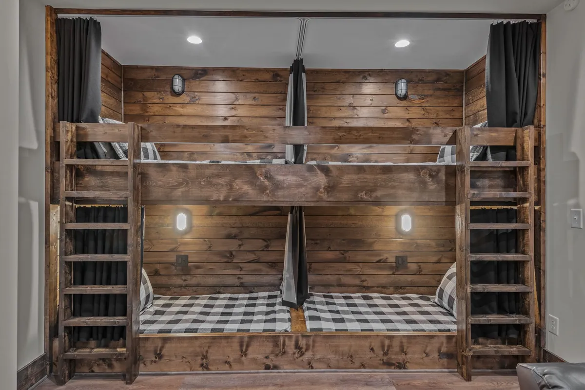 A cozy bunk room with custom-built wooden bunk beds, accented by warm wood paneling and blackout curtains for privacy. Each bunk has its own reading light, and the space feels inviting for children and families alike.