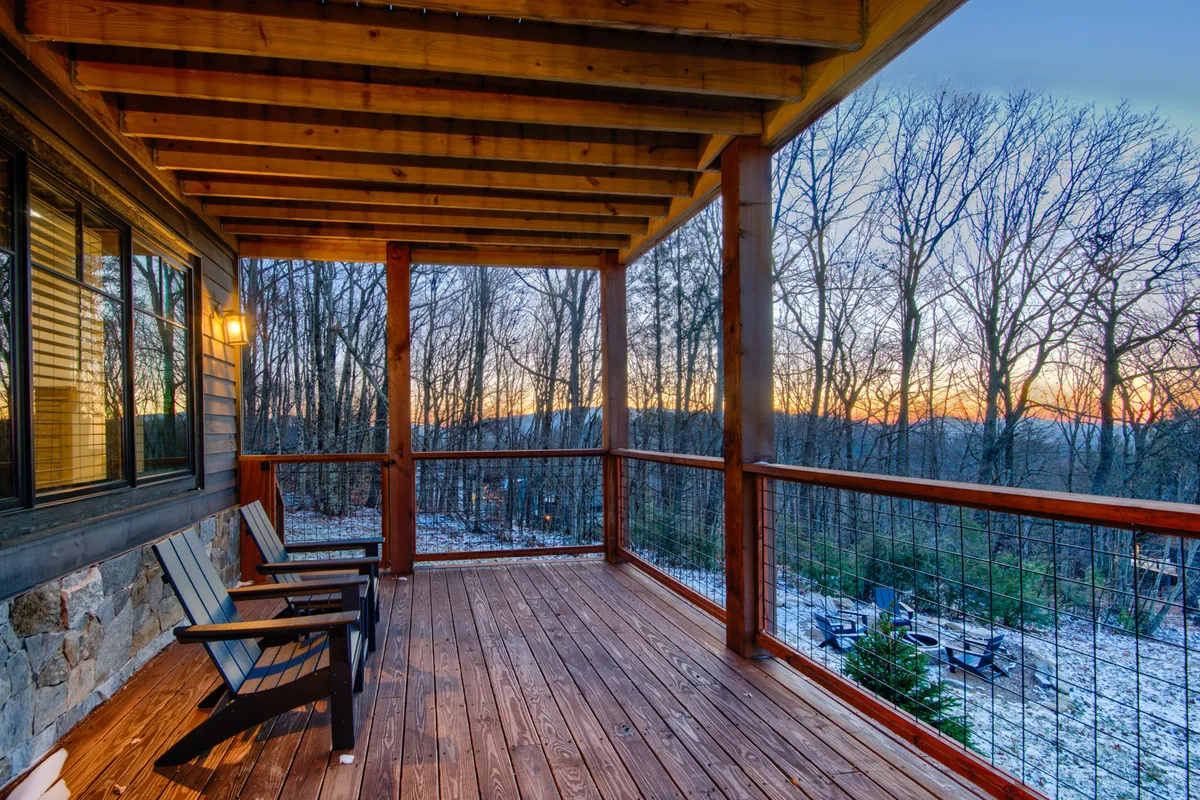 A wooden deck perched among the trees, outfitted with classic rocking chairs facing a breathtaking sunset view, offers a peaceful spot to relax after a day of outdoor activity. The surrounding trees and warm light evoke a serene connection to nature.