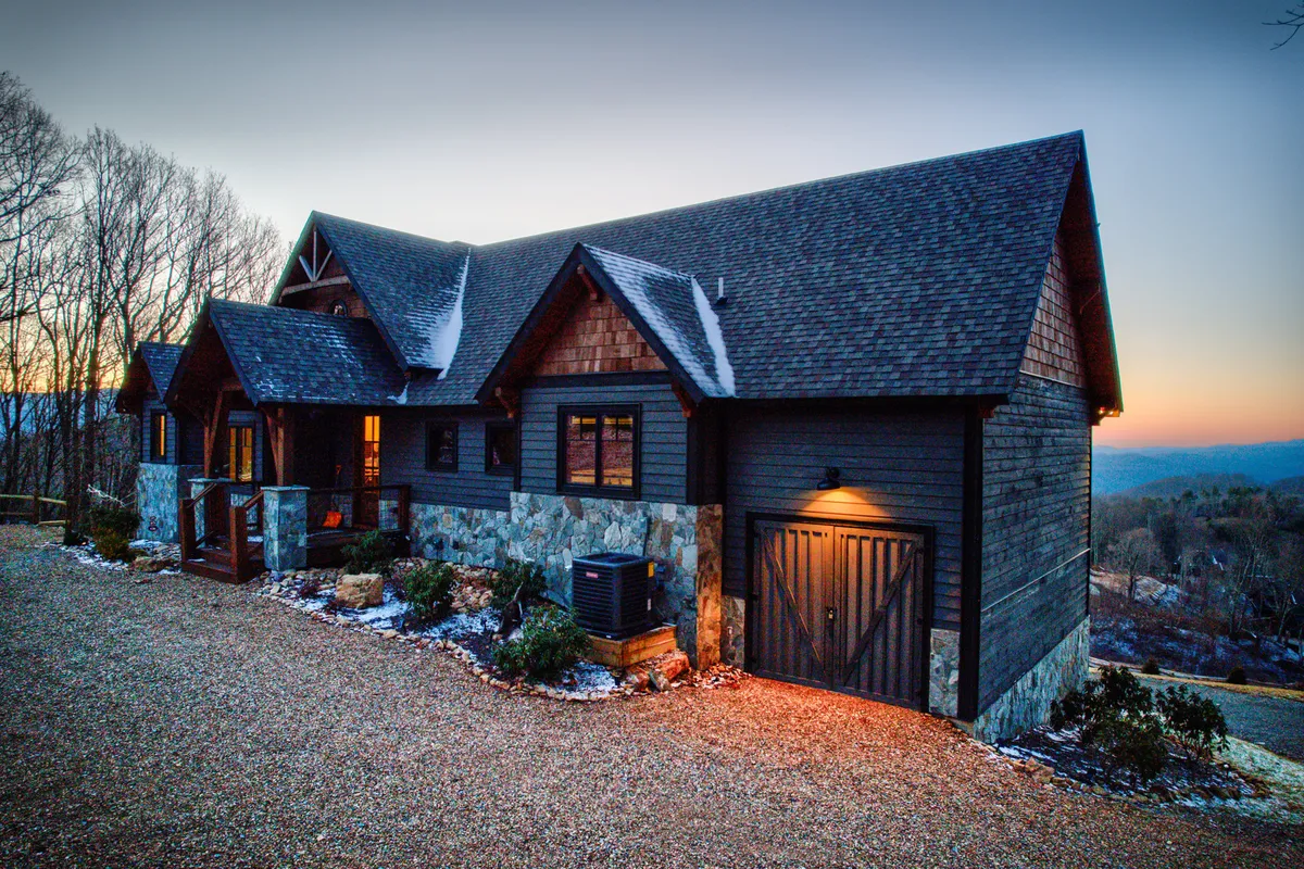 An inviting exterior shot of the property’s stone facade and warmly-lit wooden front door, with golden light spilling from the windows. The scene hints at both privacy and a welcoming, upscale retreat, with the mountains in the background alluding to the scenic setting.