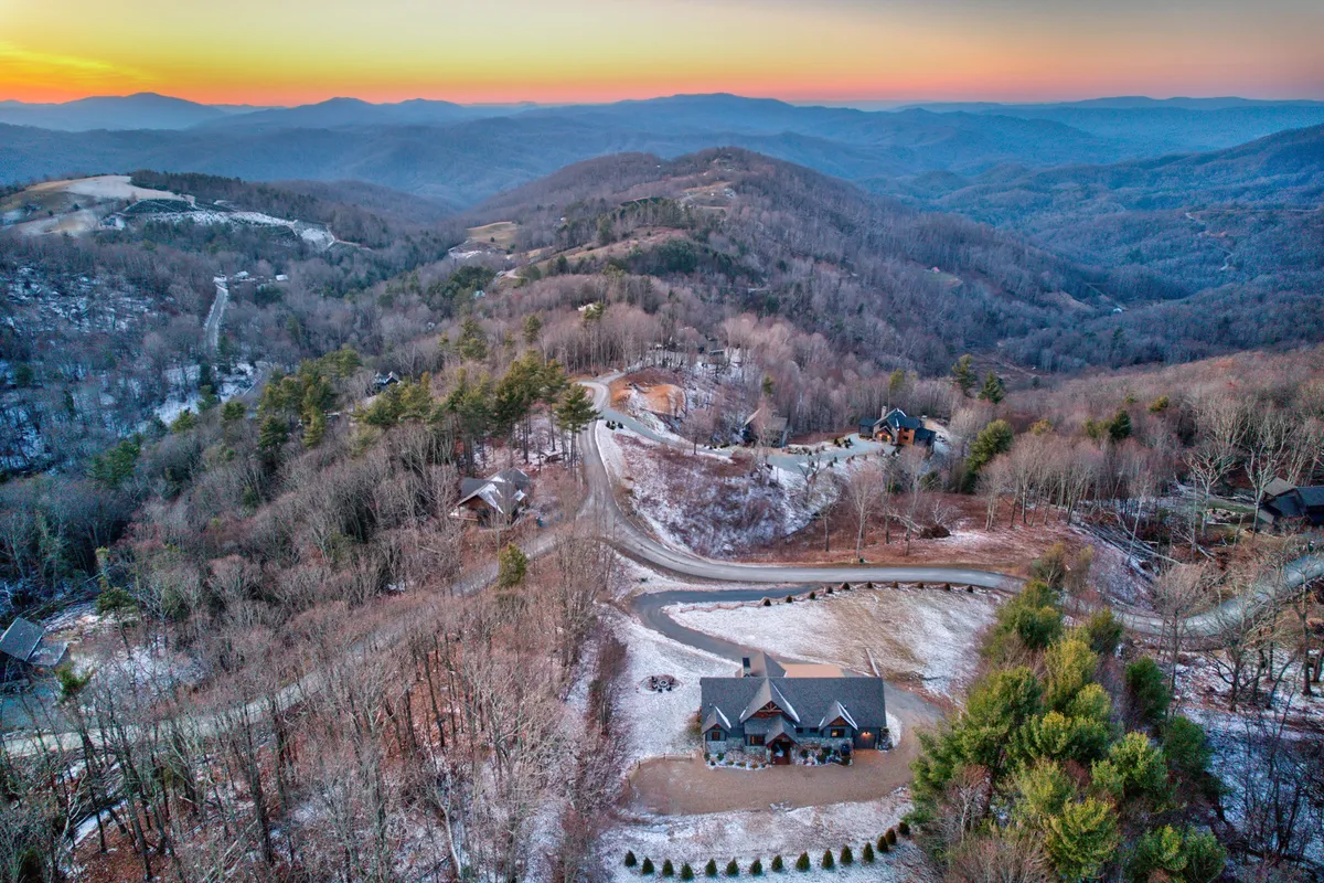 A sweeping view of a mountainous landscape surrounds the main property, with a winding road leading through the tranquil scenery. The outdoors beckons with wooded hills, open skies, and the kind of environment perfect for hiking, biking, and exploring nature.