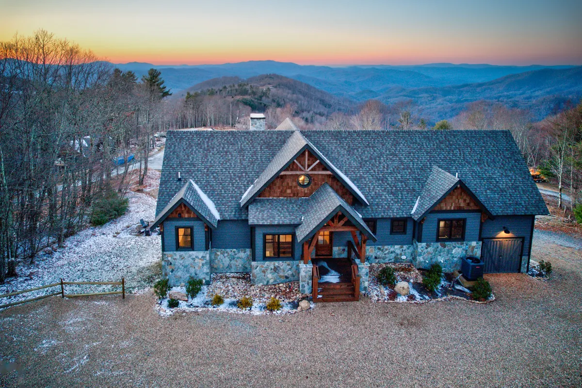 The image showcases The Tipsy Bear cabin's stunning exterior set against sweeping mountain vistas, bordered by a beautifully landscaped garden. The spacious porch invites relaxation while guests take in panoramic sunsets. The setting is peaceful and welcoming, perfectly blending luxury and nature.